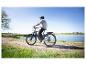 Mann auf grauem E-Bike an einem See an einem sonnigen Tag.