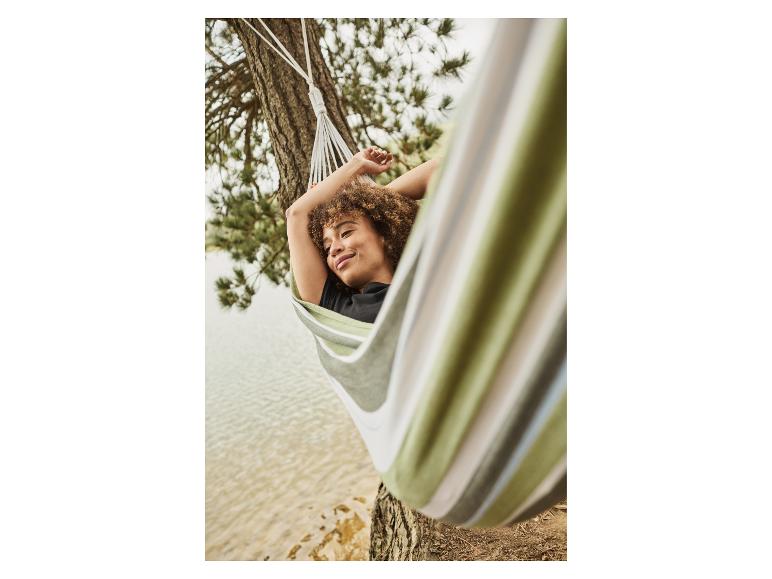 Frau entspannt sich in einer grün-beige gestreiften Hängematte am See.