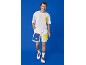 Mann in weißem T-Shirt, weißen Shorts mit farbigen Taschen und Turnschuhen.