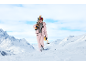 Frau im rosa Skianzug mit Skiern auf der Schulter läuft durch den Schnee.