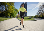 Mann in gelb-schwarzer Laufjacke und schwarzen Shorts joggt im Freien.