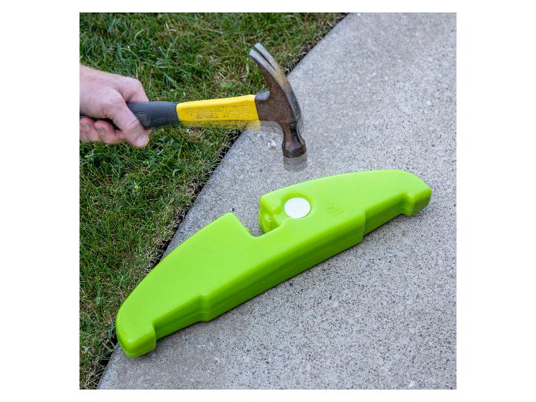 Hammer und ein grünes Plastikteil auf Beton und Gras.