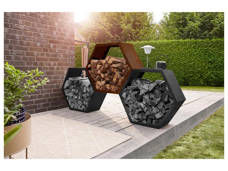 Sechseckiges Kaminholzregal auf einer Terrasse mit Ziegelwand und grüner Hecke.