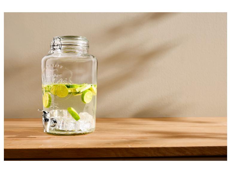 Glasgetränkespender mit Zapfhahn, gefüllt mit Wasser, Limettenscheiben und Eiswürfeln.