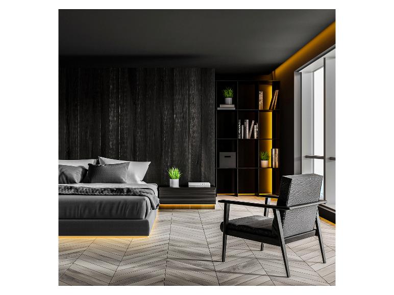 Modernes dunkles Schlafzimmer mit Bett, Sessel und Bücherregal mit dekorativer Beleuchtung.