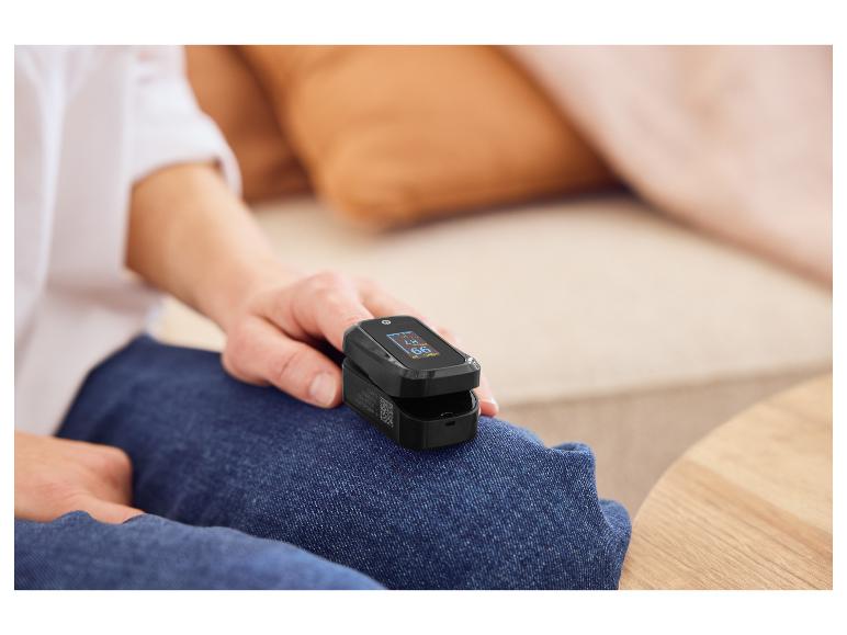 Person sitzt auf einem Sofa und misst Blutsauerstoff und Herzfrequenz mit einem Pulsoximeter.