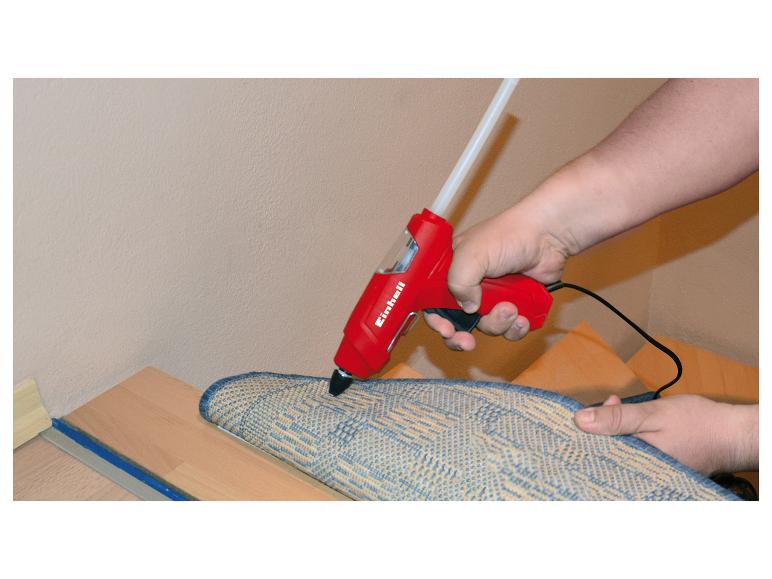 Eine Hand benutzt eine Heißklebepistole, um einen Teppich auf einem Holzfußboden zu befestigen.