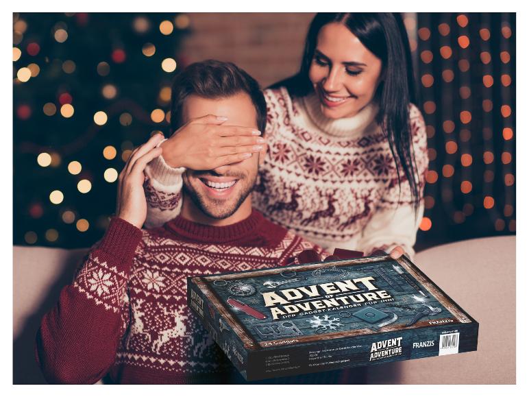 Ein lächelndes Paar, die Frau verdeckt die Augen des Mannes, während er einen Franzis Advent of Adventure Adventskalender hält.