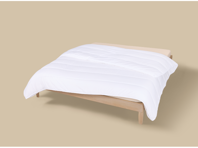 Weiße Bettdecke auf einem hellen Holzbett mit beiger Bettwäsche.
