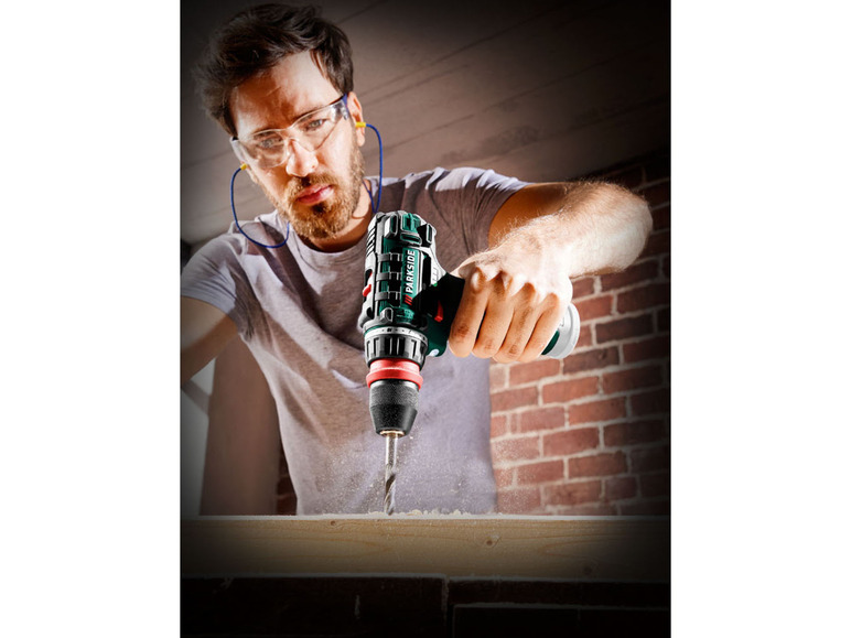 Ein Mann bohrt mit einer grünen Parkside Bohrmaschine in Holz.