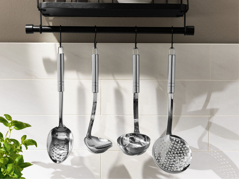 Ein Satz Küchenutensilien, darunter eine Suppenkelle, ein Schöpflöffel und ein Schaumlöffel, hängen an einer schwarzen Schiene.