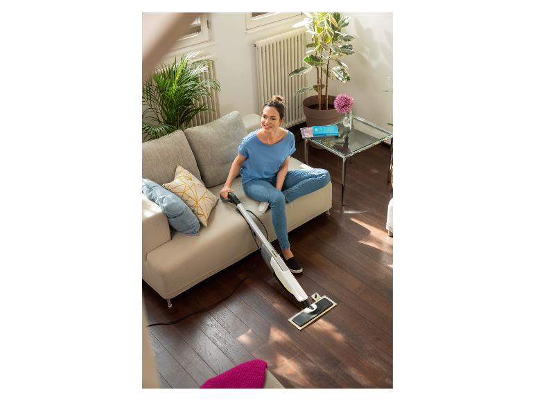 Frau auf einem Sofa reinigt einen Holzboden mit einem Bodenreiniger.