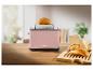 Rosa Toaster mit Brötchen auf einem Holztisch, ein Brötchen oben auf dem Toaster.