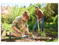 Eine Frau und ein Mann arbeiten im Garten mit einer Harke und Handwerkzeugen.