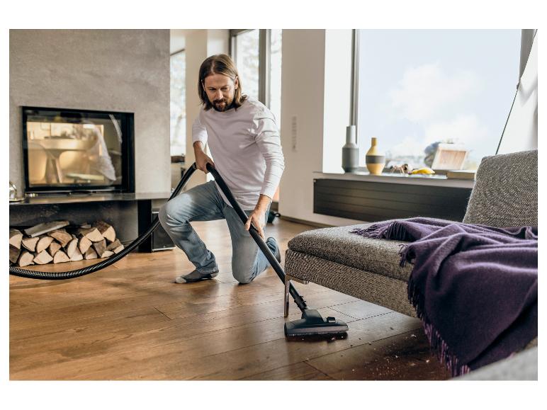Mann saugt Holzboden in modernem Wohnzimmer mit Kamin.