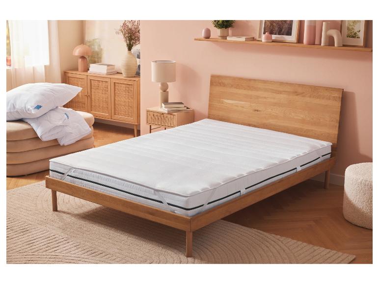 Weißer Matratzentopper auf einem Holzbett in einem Schlafzimmer mit rosa Wänden.