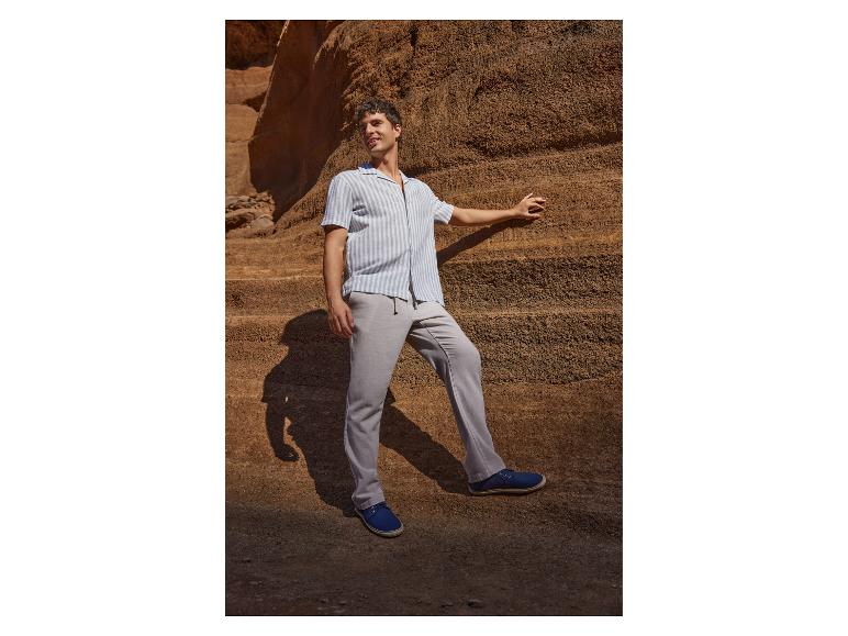 Mann in gestreiftem Hemd und grauer Hose posiert an einer Felswand.