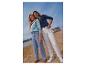 Zwei Frauen in Jeans und Shirts am Strand, mit Boot und Meer im Hintergrund.