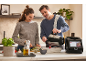 Ein Paar kocht mit einer Küchenmaschine und gießt Zutaten in eine Auflaufform.