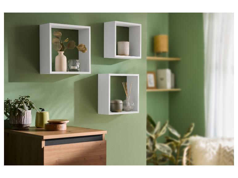 Weiße Wandregale mit Dekorationen an einer grünen Wand, darunter eine Holzkommode.