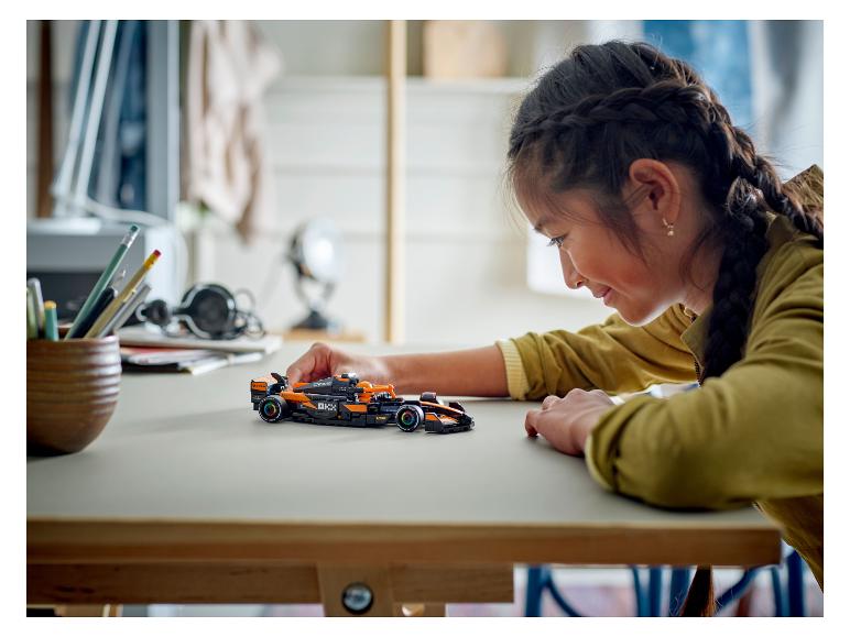 Ein Mädchen betrachtet einen schwarz-orangen LEGO Speed Champions McLaren Formel-1-Rennwagen.