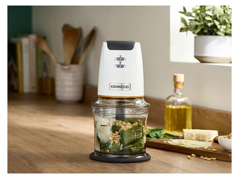 Weißer Zerkleinerer mit Pesto-Zutaten auf einer Holzküchenarbeitsplatte.