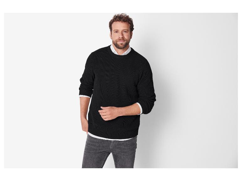 Ein Mann in einem schwarzen Pullover und grauen Jeans.