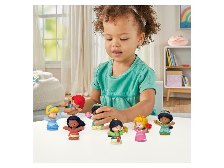 Ein kleines Kind spielt mit einer Sammlung von Prinzessinnenfiguren auf einem weißen Tisch.