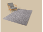 Holzsessel mit grauen Kissen und grauem Teppich mit geometrischem Muster.