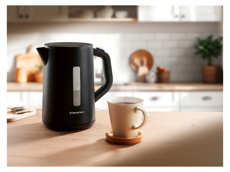 Ein schwarzer SilverCrest Wasserkocher steht auf einem Holztisch neben einer Tasse Tee.