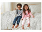 Zwei Kinder im Schlafanzug, ein Junge in einem blau karierten Pyjama mit Weltraum-Motiv und ein Mädchen in einem rosa gepunkteten Pyjama.