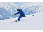Kind in blau-schwarzer Skikleidung, Helm und Brille, beim Skifahren auf einer verschneiten Piste.