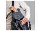 Person in cremefarbenem Pullover steckt graue Tasche in schwarze Leder-Umhängetasche.