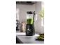 Mixer mit grünem Smoothie auf einer Küchenarbeitsplatte, daneben geschnittene Limetten und Nüsse.