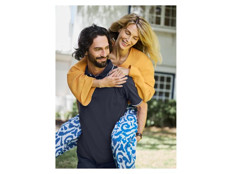 Glückliches Paar in Freizeitkleidung: Sie trägt ein orangefarbenes Kleid, er ein schwarzes Polohemd und eine blaue Hose.