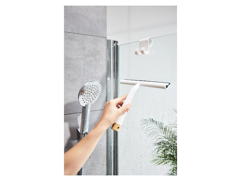 Eine Hand, die einen weißen Duschwischer benutzt, um eine gläserne Duschwand zu reinigen.