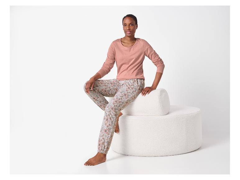 Frau in rosa Langarmshirt und floraler Pyjamahose, sitzend auf einem weißen Hocker.