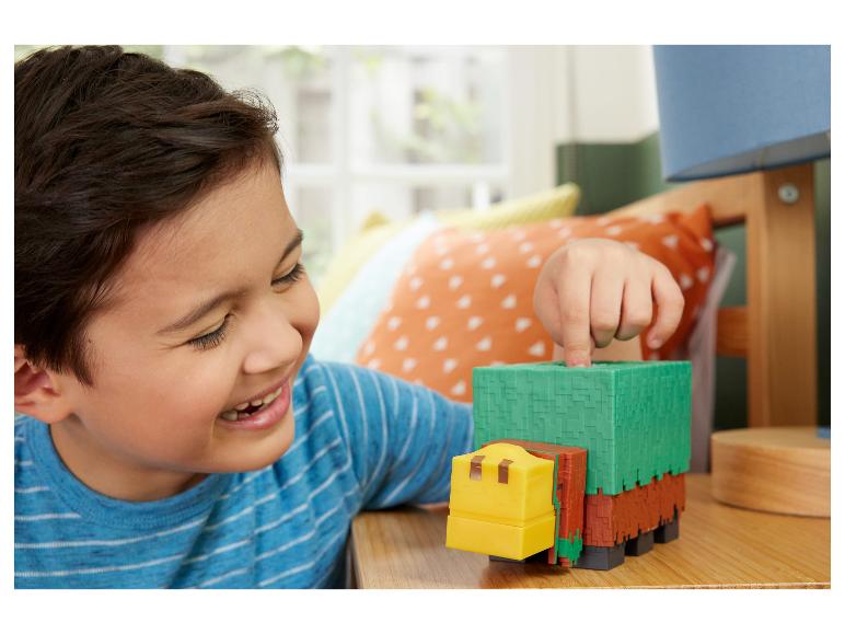 Ein lächelndes Kind spielt mit einem blockartigen, grün-braunen Spielzeuglastwagen auf einem Holztisch.