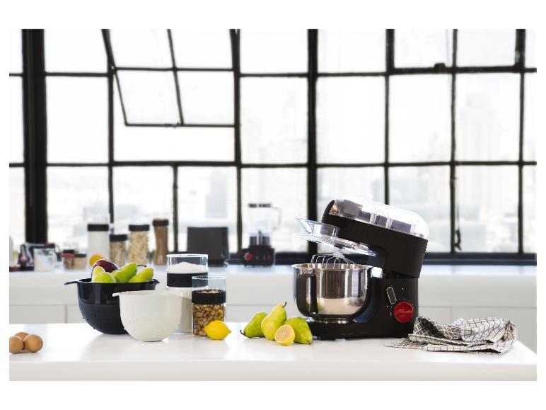 Küchenmaschine und Küchenutensilien auf einer weißen Arbeitsplatte vor einem Fenster.