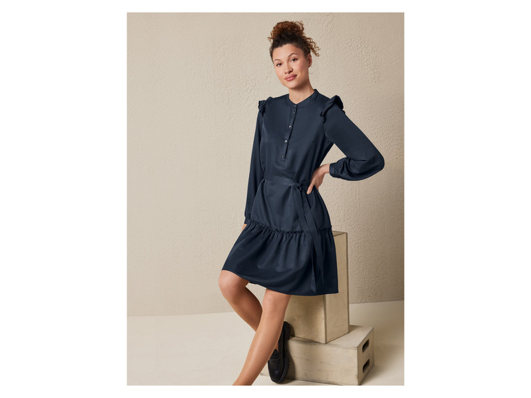 Eine Frau trägt ein dunkelblaues Kleid mit Rüschen und Gürtel.