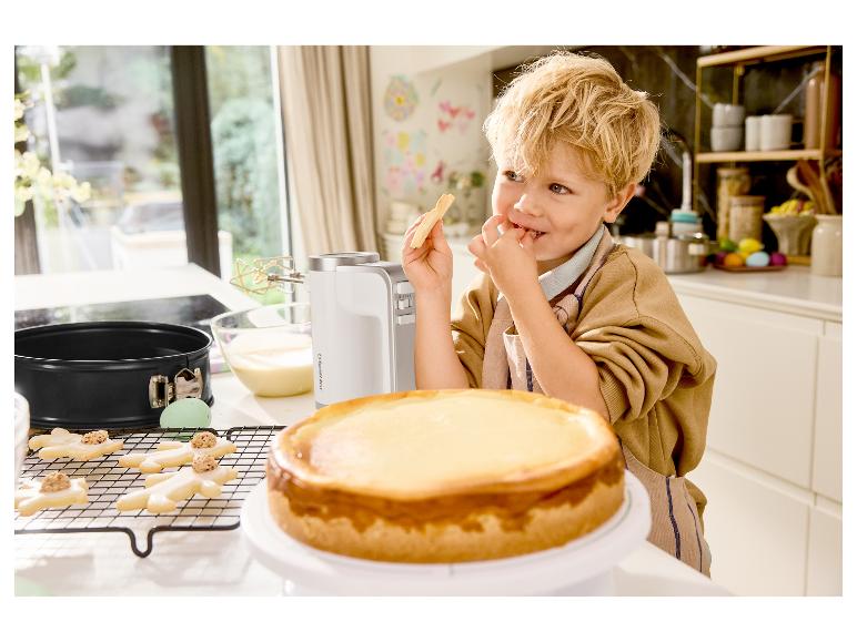 Junge isst Keks neben Silvercrest Mixer und Käsekuchen in der Küche
