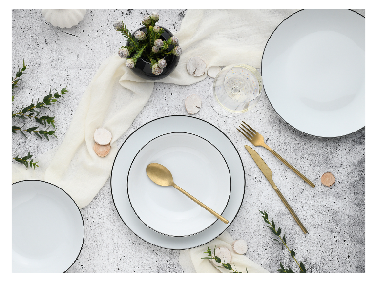Weißes Geschirr mit schwarzem Rand, goldenes Besteck, minimalistische Dekoration.