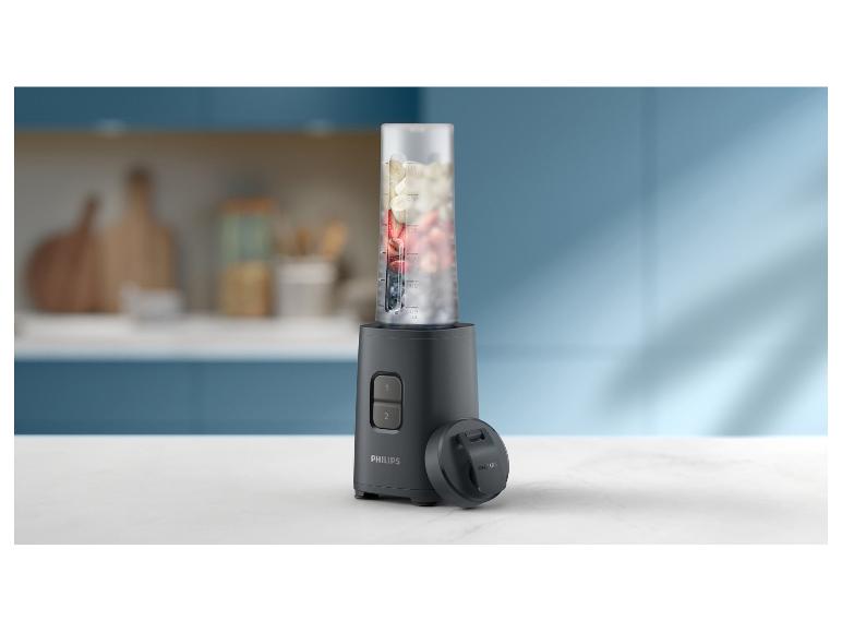 Schwarzer Mixer mit Früchten und Deckel auf einer Küchenarbeitsplatte.