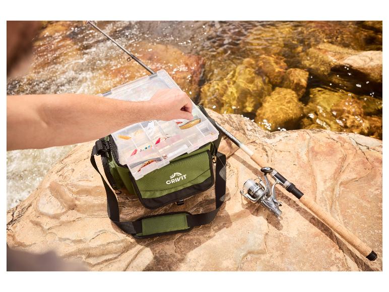 Mann wählt Köder aus einer Angelbox, neben Angelrute und Rolle auf einem Felsen am Fluss.