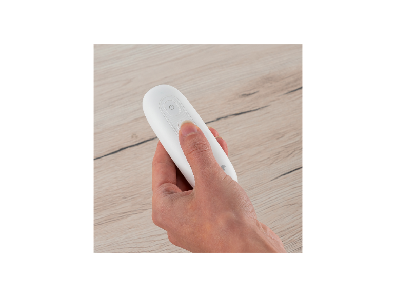 Eine Hand hält eine weiße Fernbedienung mit einem Einschaltknopf auf einer Holzoberfläche.