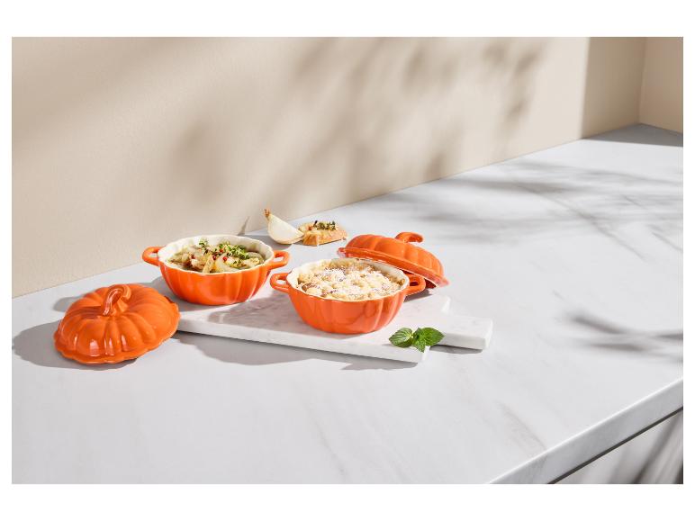 Zwei orangefarbene kürbisförmige Auflaufformen mit Essen auf einer Marmorplatte.