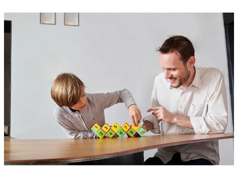 Vater und Kind spielen mit nummerierten Bausteinen auf einem Holztisch.