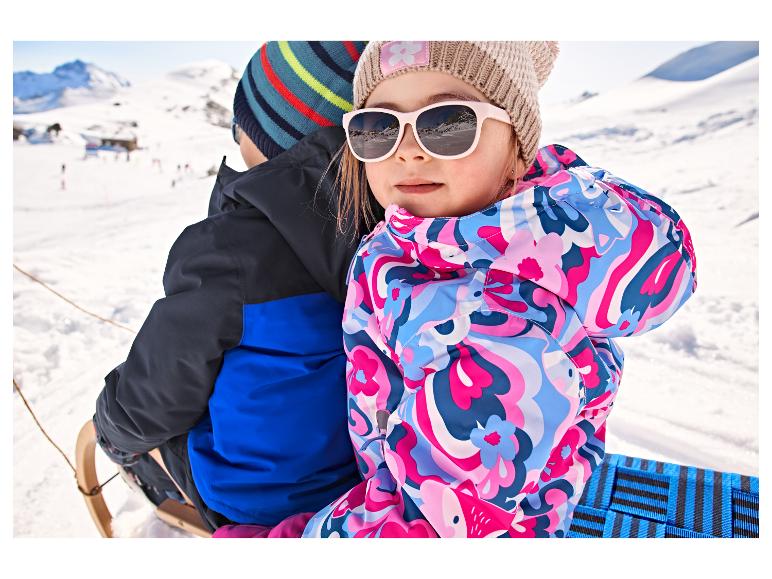 Kleinkind in einer bunten LUPILU® Schneejacke auf einem Schlitten im Schnee