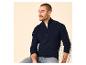Mann in einem marineblauen Pullover mit Reißverschluss und Jeans, auf einem Stuhl sitzend.