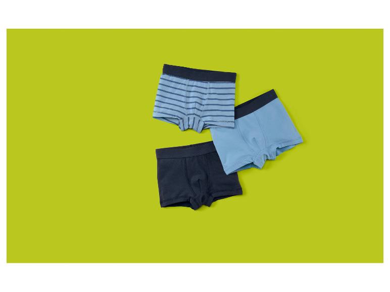 Drei Jungen-Boxershorts in Blau und Marineblau, eine gestreift, auf limettengrünem Hintergrund.